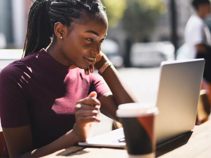 A young black woman looks intently at her laptop while out on a sunny day