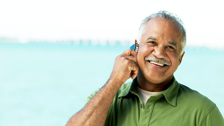 A Hispanic man smiles while talking on a cell phone outside