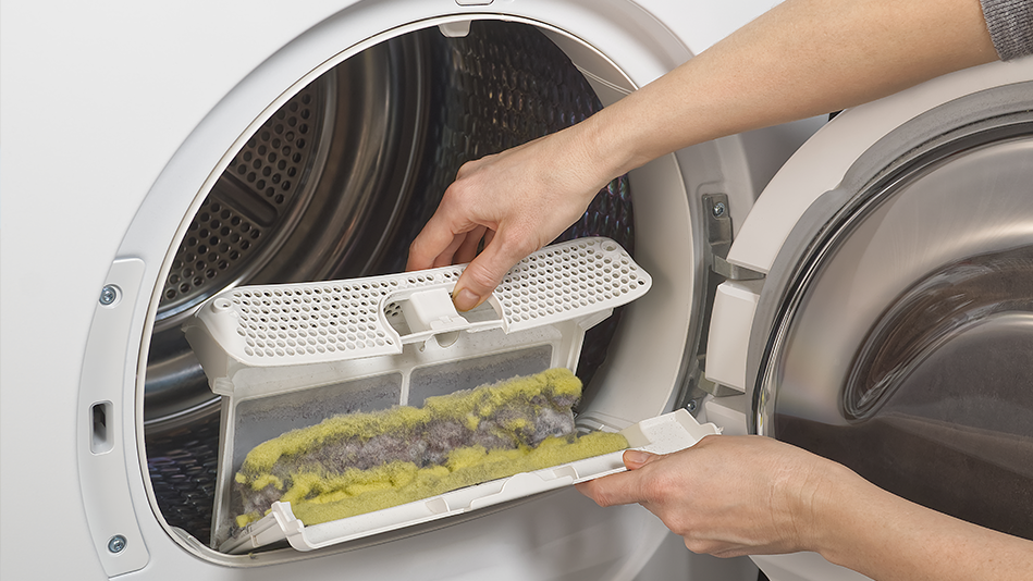 A light-skinned pair of hands pulls a full lint screen from a white dryer