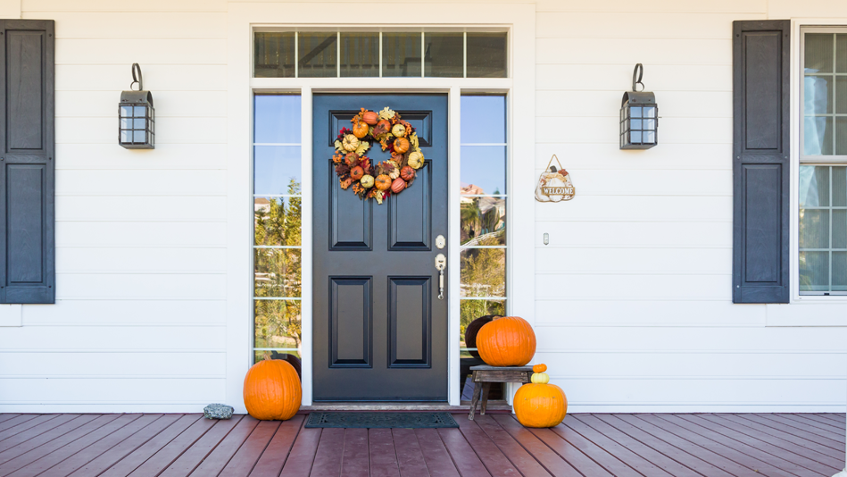 A teal-and-white front porch is adorned with a fall wreath and assorted pumpkins