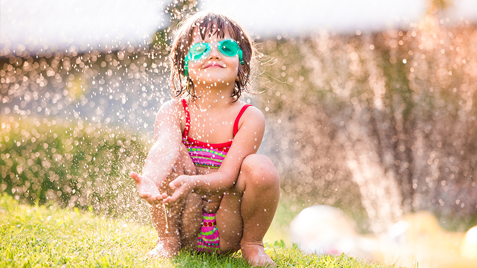 A little girl plays in the water coming from a sprinkler