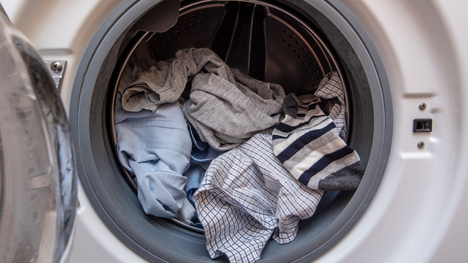A white dryer sits open and half-full of gray, blue, white, and black clothing