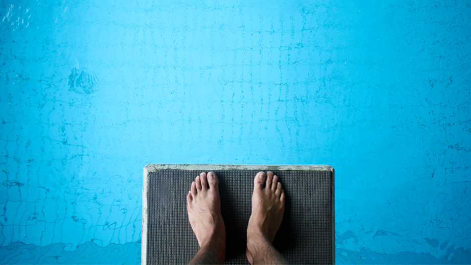 Feet stand on the end of a diving board above a pool