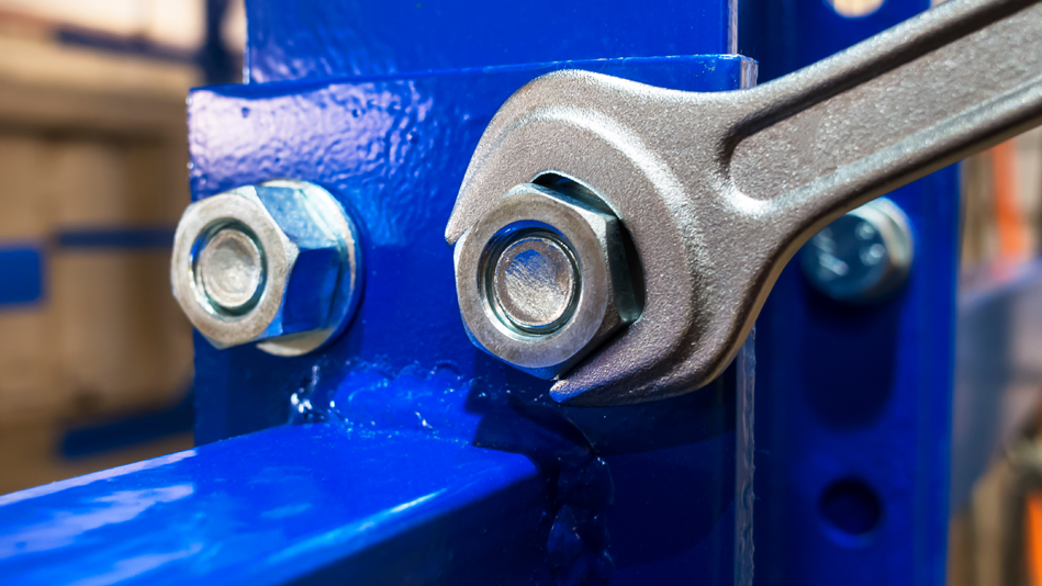 A wrench tightens a bolt on a blue metal stand