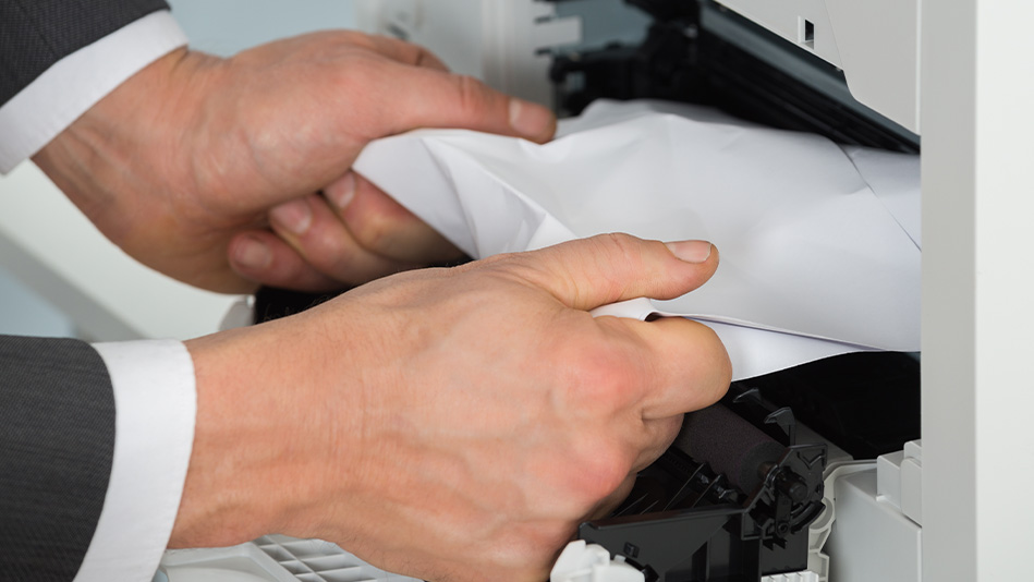 White hands emerging from two suit sleeves pull on paper jammed in a printer