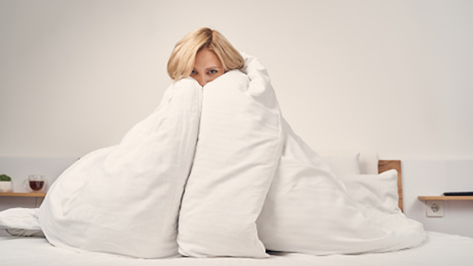 A white woman cozies up inside a white down alternative comforter