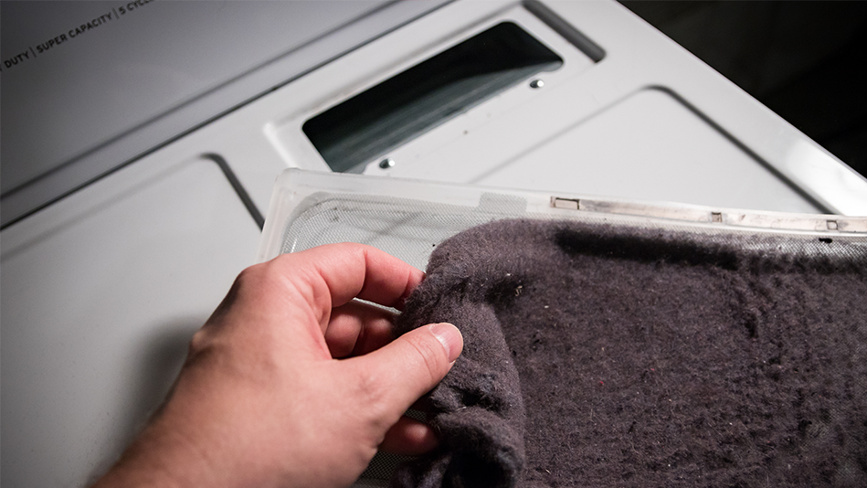 A hand pulls lint out of a clothes dryer lint trap