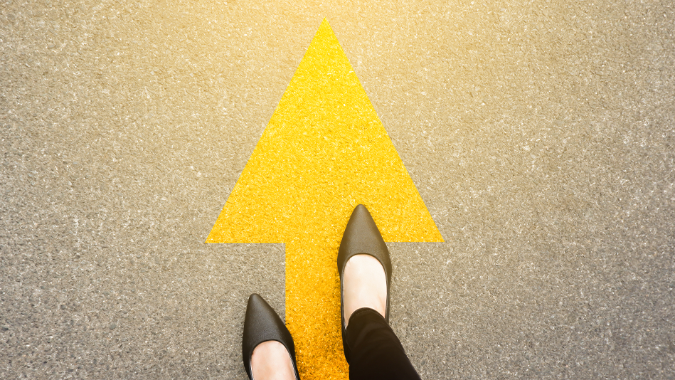 A woman's feet follow the direction of a yellow arrow on pavement