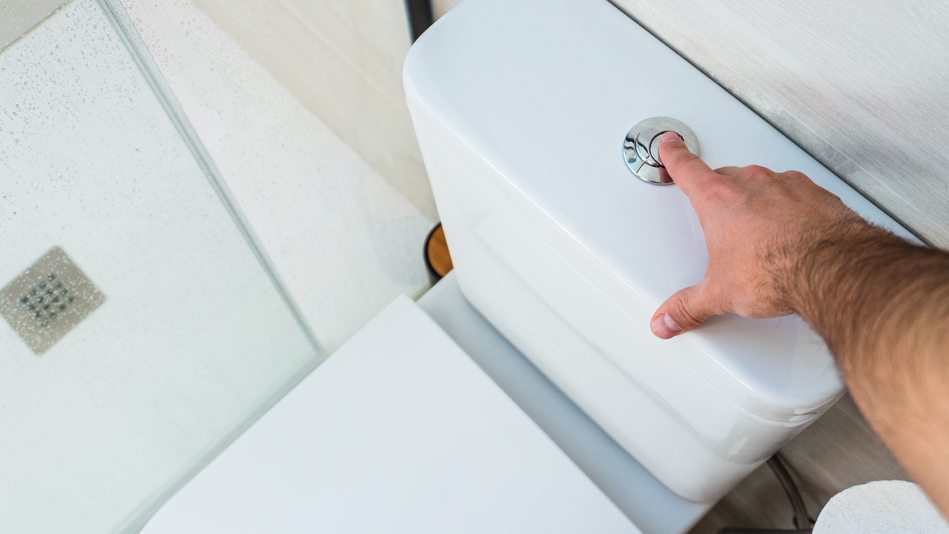 An adult right hand presses one button on a white dual-flush toilet