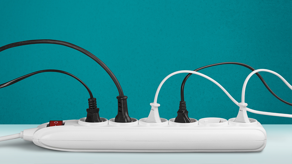 3 black cords and 2 white cords are plugged into a power strip on a white table in front of a teal wall