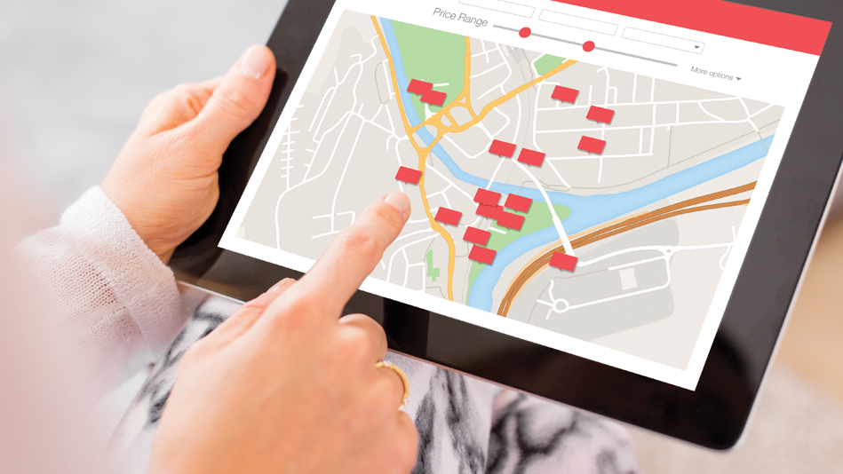 Hands holding a tablet with right hand pointing to a red square site on a digital map