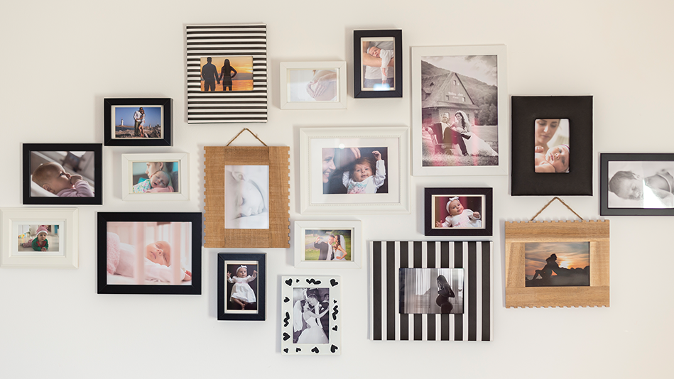 Assorted photo frames hang on a beige wall with 1-2 people in each photo at different life stages