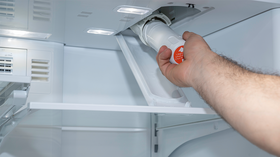A hand removes the water filter from a refrigerator