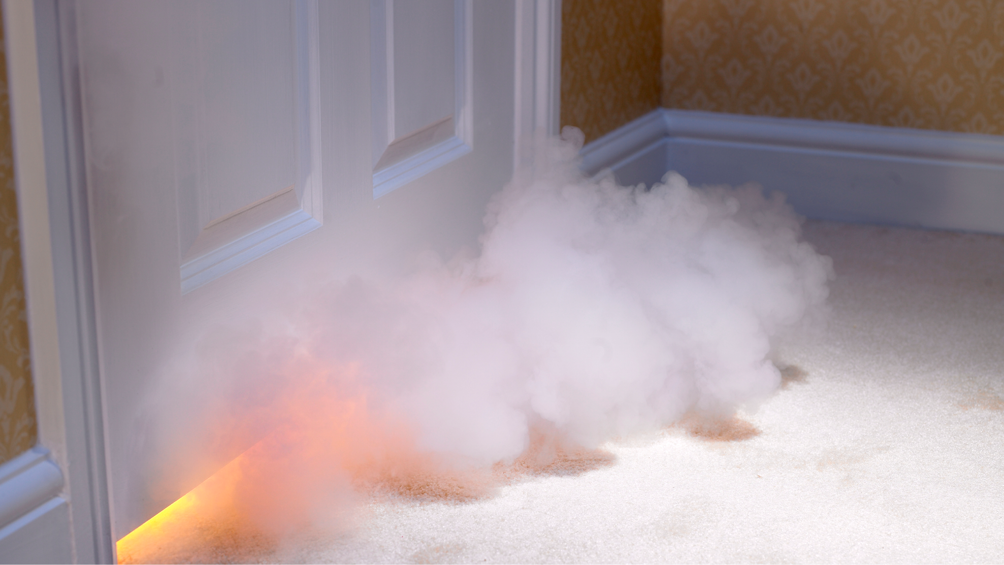 White smoke emerges from the fire under a white door inside a home