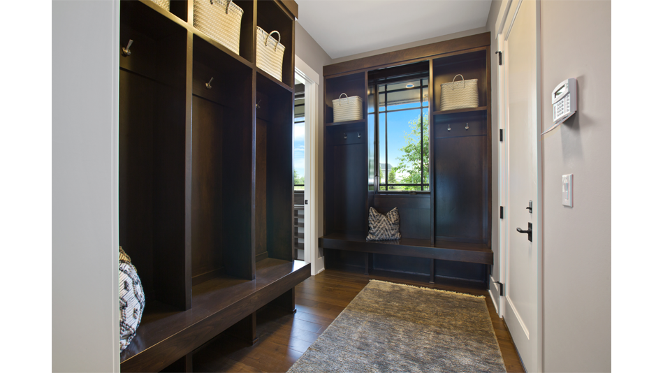 A mudroom features perpendicular dark wood mudroom lockers, with black-and-white pillows on the bottom and white straw totes at the top of each locker. There is a window in the middle of the second mudroom locker wall. 