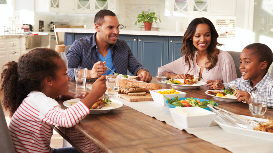 A Black family (mom, dad, daughter, son) enjoys a nice, fresh lunch in the sunny, spacious kitchen of their new construction home
