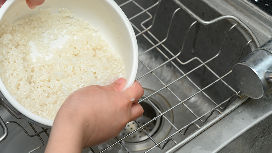 Hands hold a bowl of rice over a grated sink