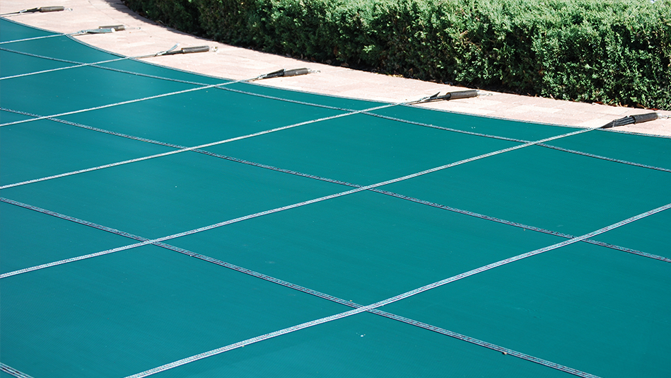 Open your pool: A green pool cover is strapped on top of an inground pool