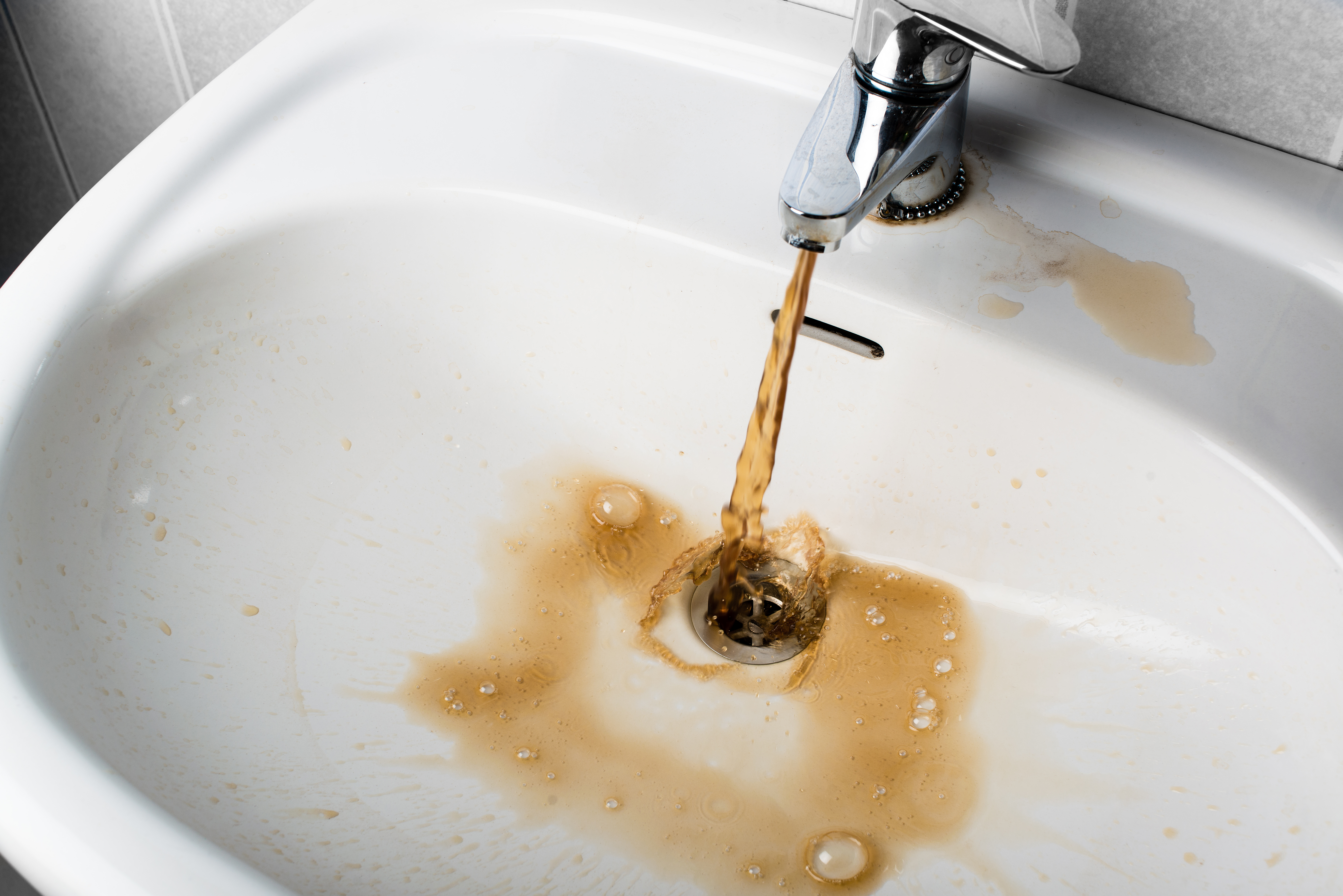 Brown water flows out of a leaky faucet into a white sink