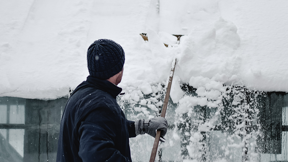 Man uses a roof rake to remove snow, causing a small avalanche
