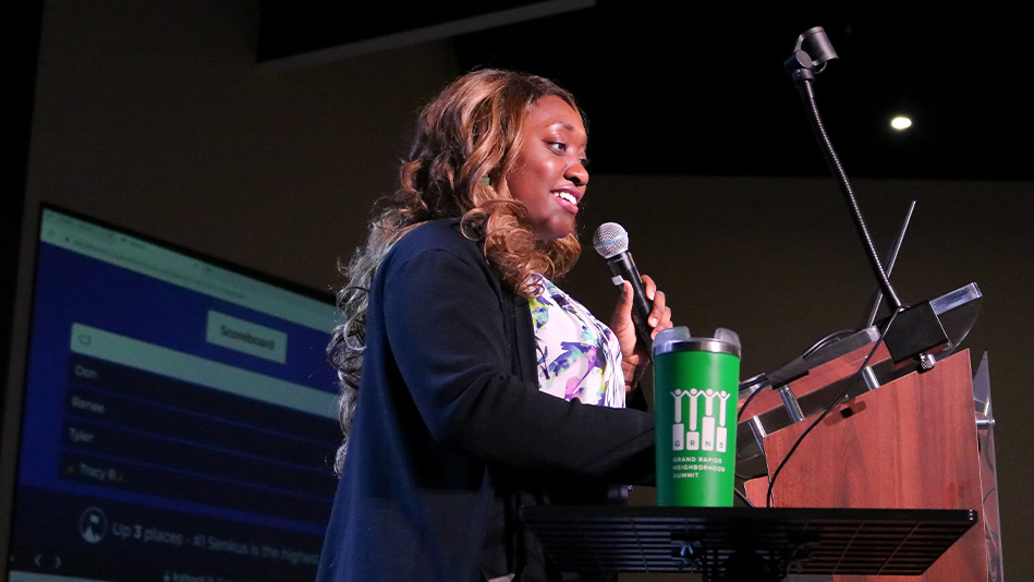 A young black woman stands behind a podium with a microphone to lead a fundraiser