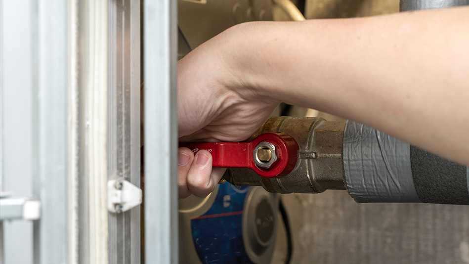 A hand grips the red handle of a pipe valve to open it