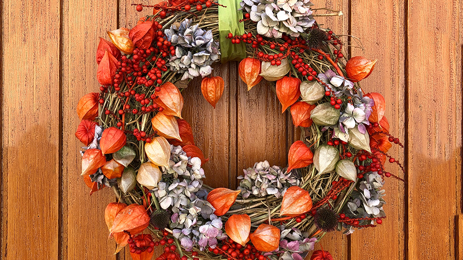 A Christmas wreath with red holly and leaves, purplish-white flowers, and lime green ribbon