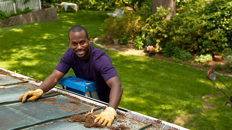 A black male adult smiles while wearing work gloves for gutter cleaning