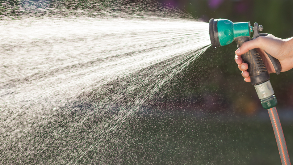 A hose sprays water as a hand squeezes the nozzle