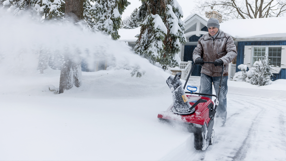 A man uses a snowblower on his driveway