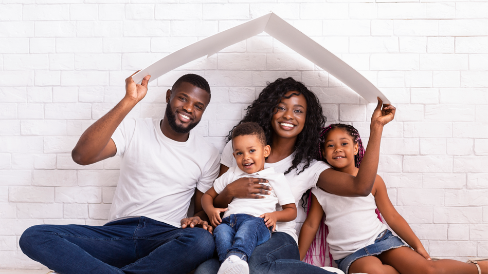 A black family in white t-shirts and jeans smile while holding a folded piece of paper overhead like a roof
