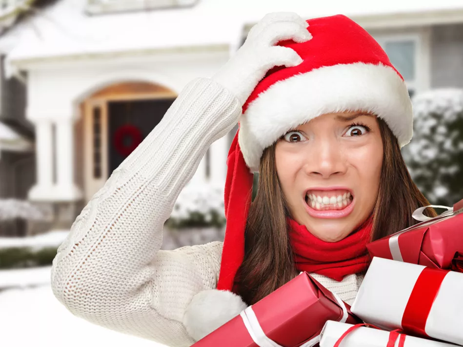 Asian/Pacific Islander woman cringes while holding her red and white Santa hat with her right hand and a pile of red and white gifts in front of a snow-covered white house