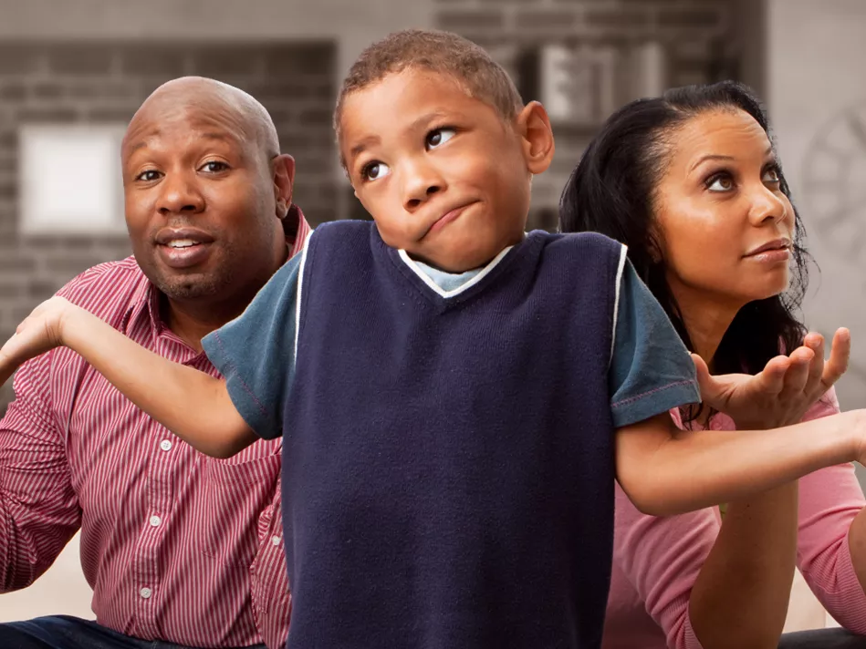 Black man on the left and Black woman on the right (both wearing red shirts) with a black boy in a blue shirt in the middle with his hands and mouth positioned to suggest, "I don't know."