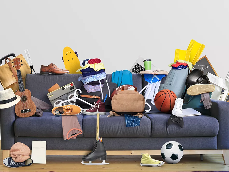Gray couch with assorted household items and on and in front of it