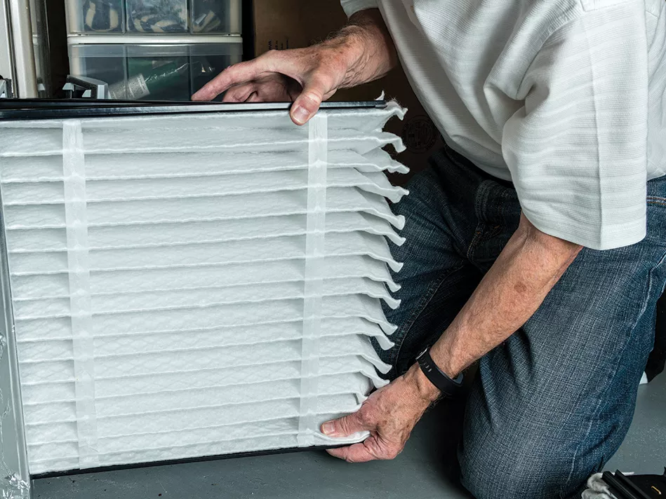 White man in a white shirt and jeans holding a furnace filter