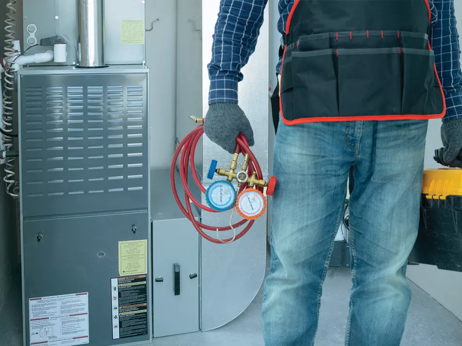 A person in a dark coat and jeans with a wound orange cord in their left hand standing next to a furnace