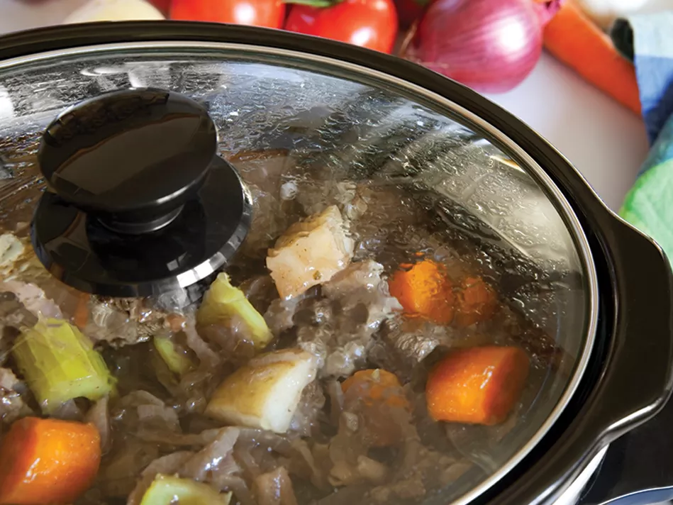 a closeup of a black crockpot with a transparent showing meat and vegetables