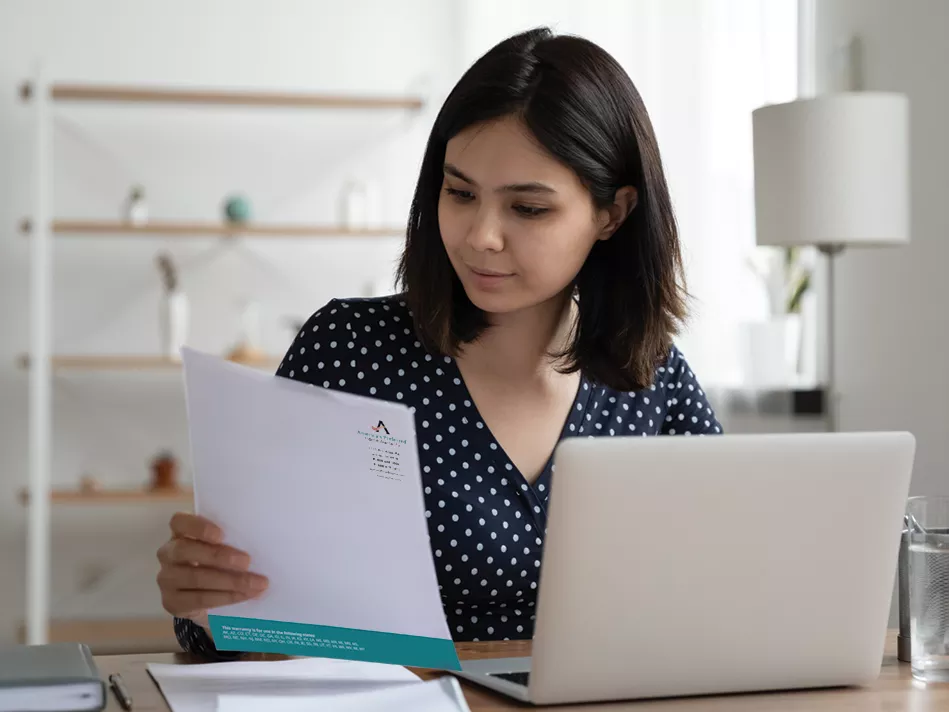 Young Hispanic woman reviews an America's Preferred Home Warranty brochure in front of her laptop