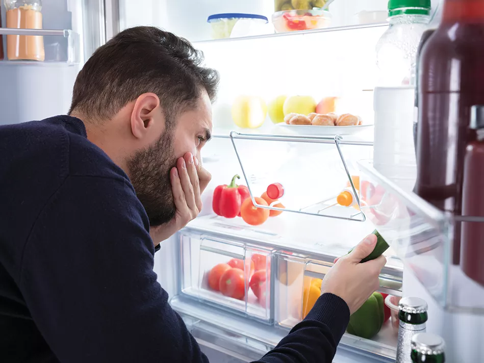 Hispanic man covers nose with left hand in front of open white refrigerator