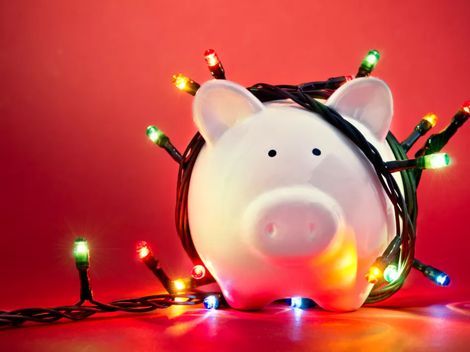 Pink piggy bank with 2 black painted dots for eyes is wrapped in a string of multicolored Christmas lights