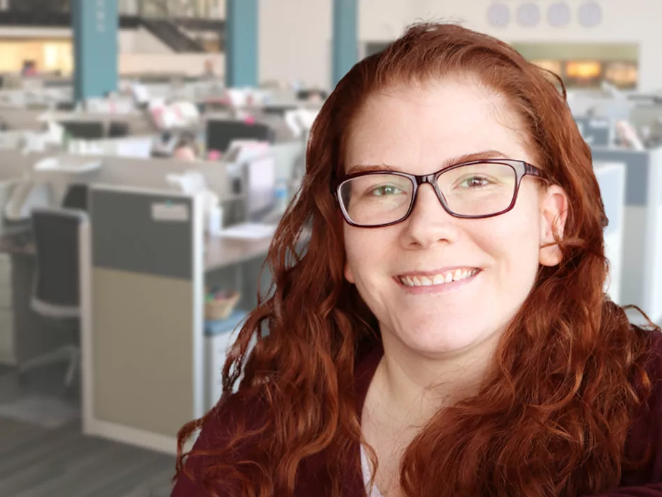 Red-haired white woman in glasses smiles in front of her office