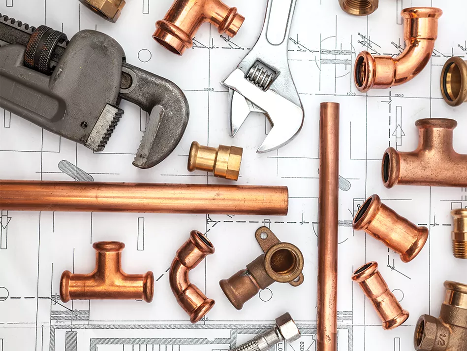 An array of pipes and piping joints are joined by 2 wrenches on top of a black-and-white blueprint