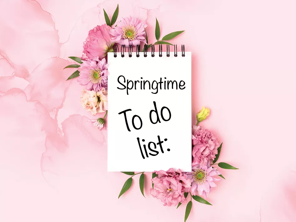 An open white notepad reads "Springtime To do list:" on a bed of pink flowers on a pink marble background