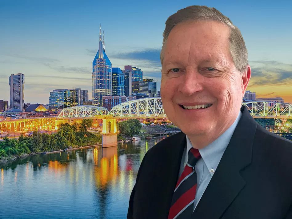 White male in a business suit smiles in front of the Nashville city skyline