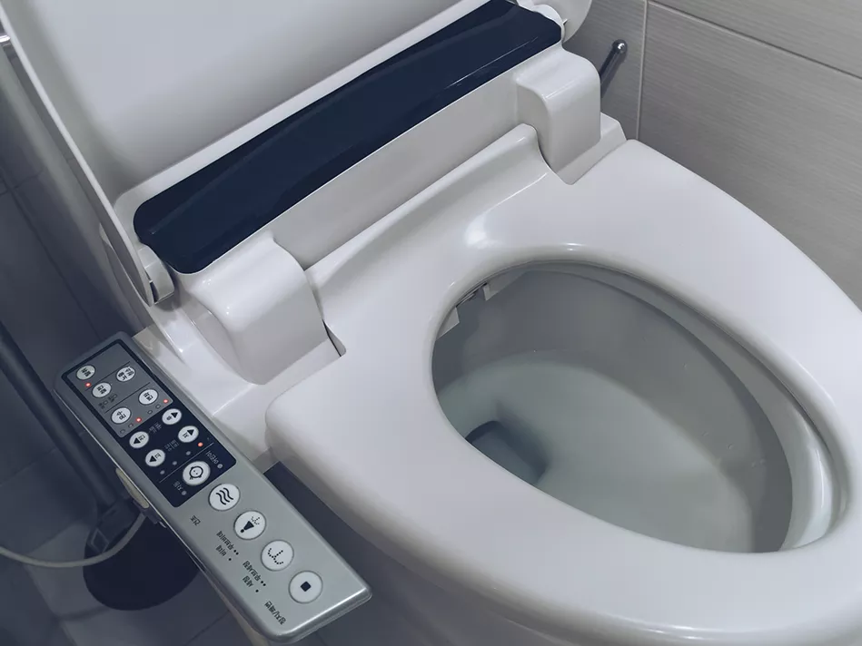 a white toilet with a gray remote for a bidet attachment