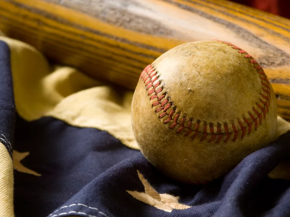 An old baseball rests next to a bat on top of an American flag
