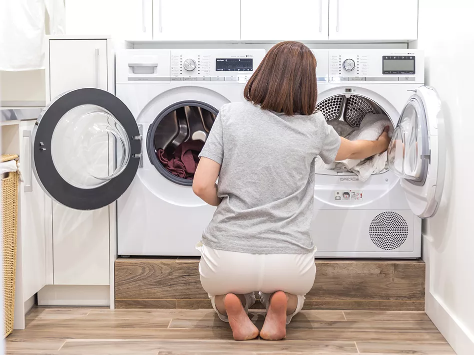 A woman kneels to transfer clothing from a front load washer into a front load dryer
