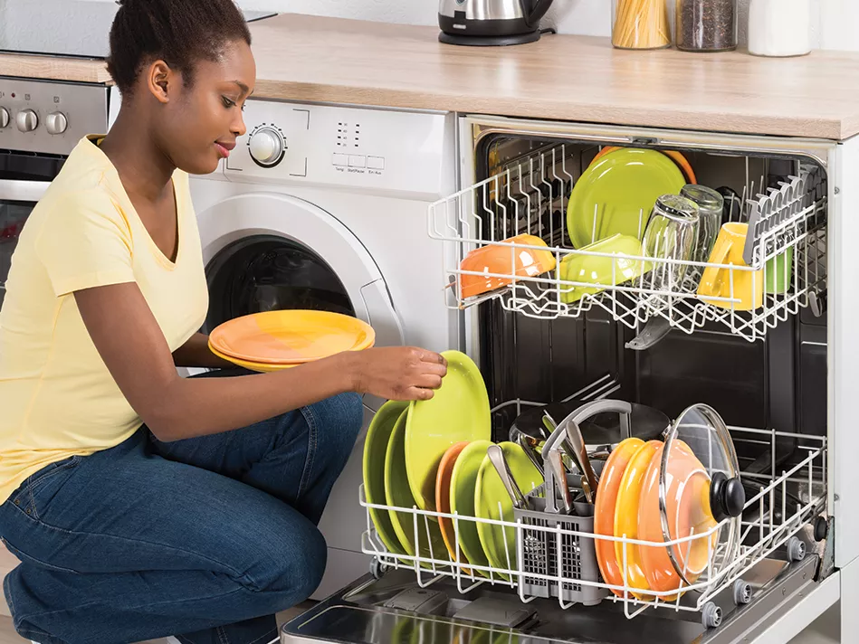 A Black woman loads a dishwasher full of citrus-colored plates