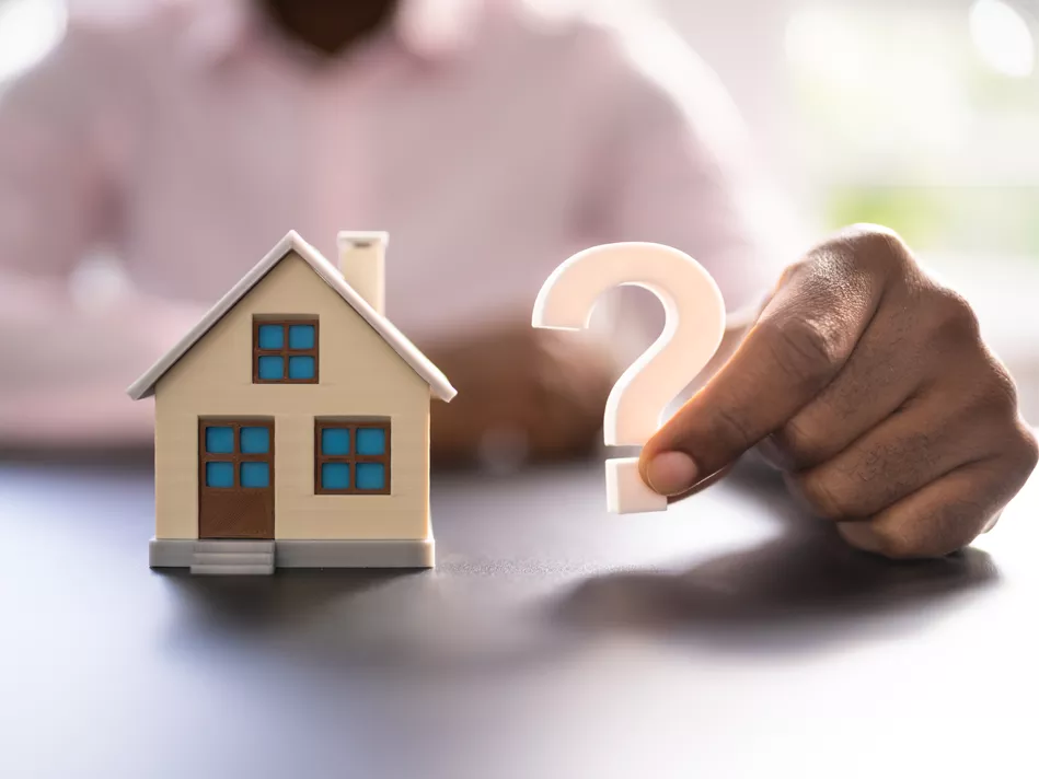 A man's hand holds a question mark next to a model of a house