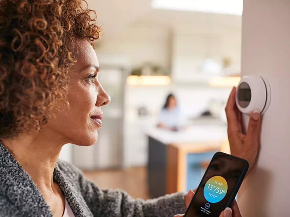 A black woman adjusts the temperature on a smart thermostat with her phone